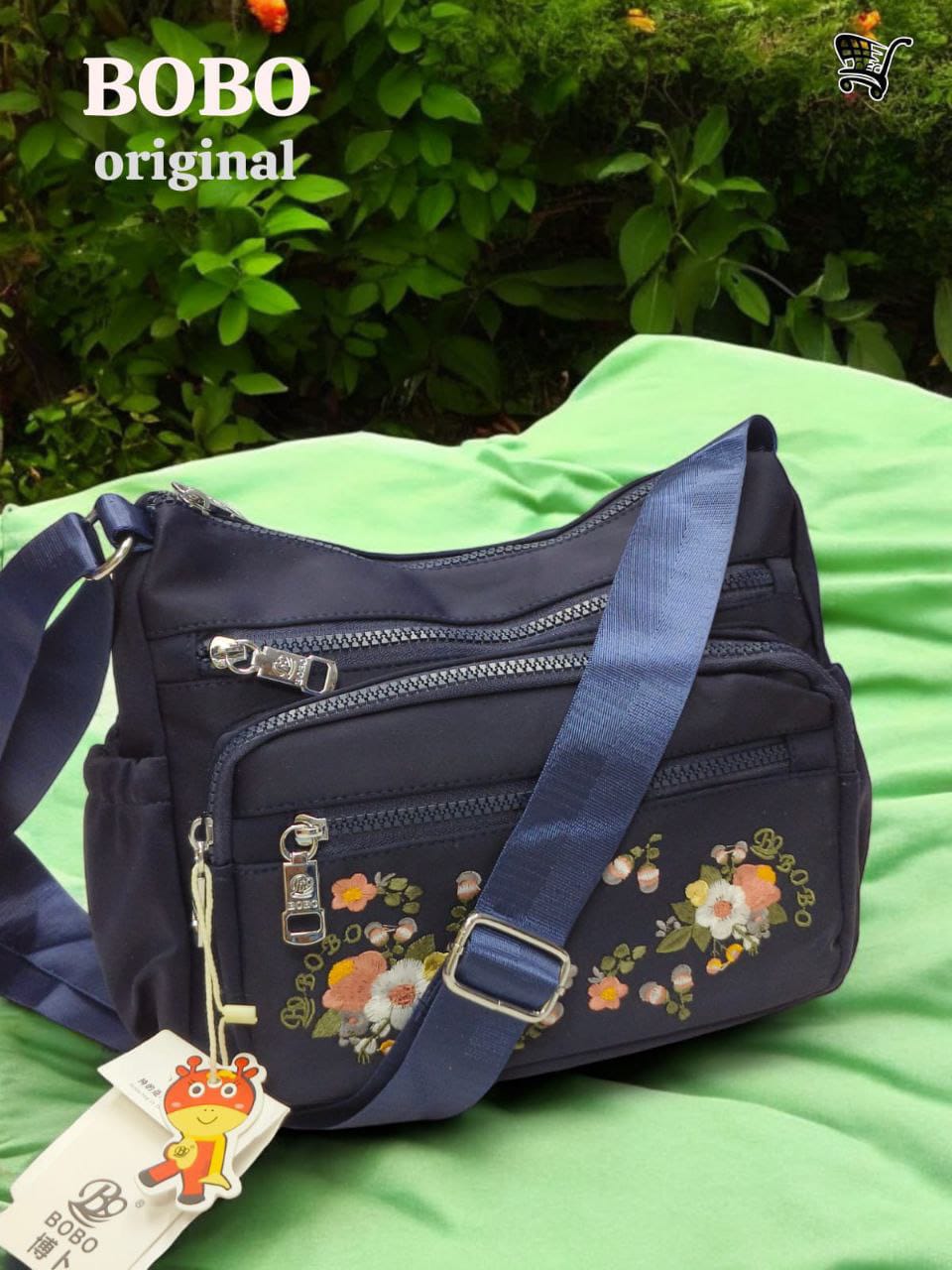 TRENDBUY BOBO Original navy blue floral bag on green fabric in a lush outdoor setting