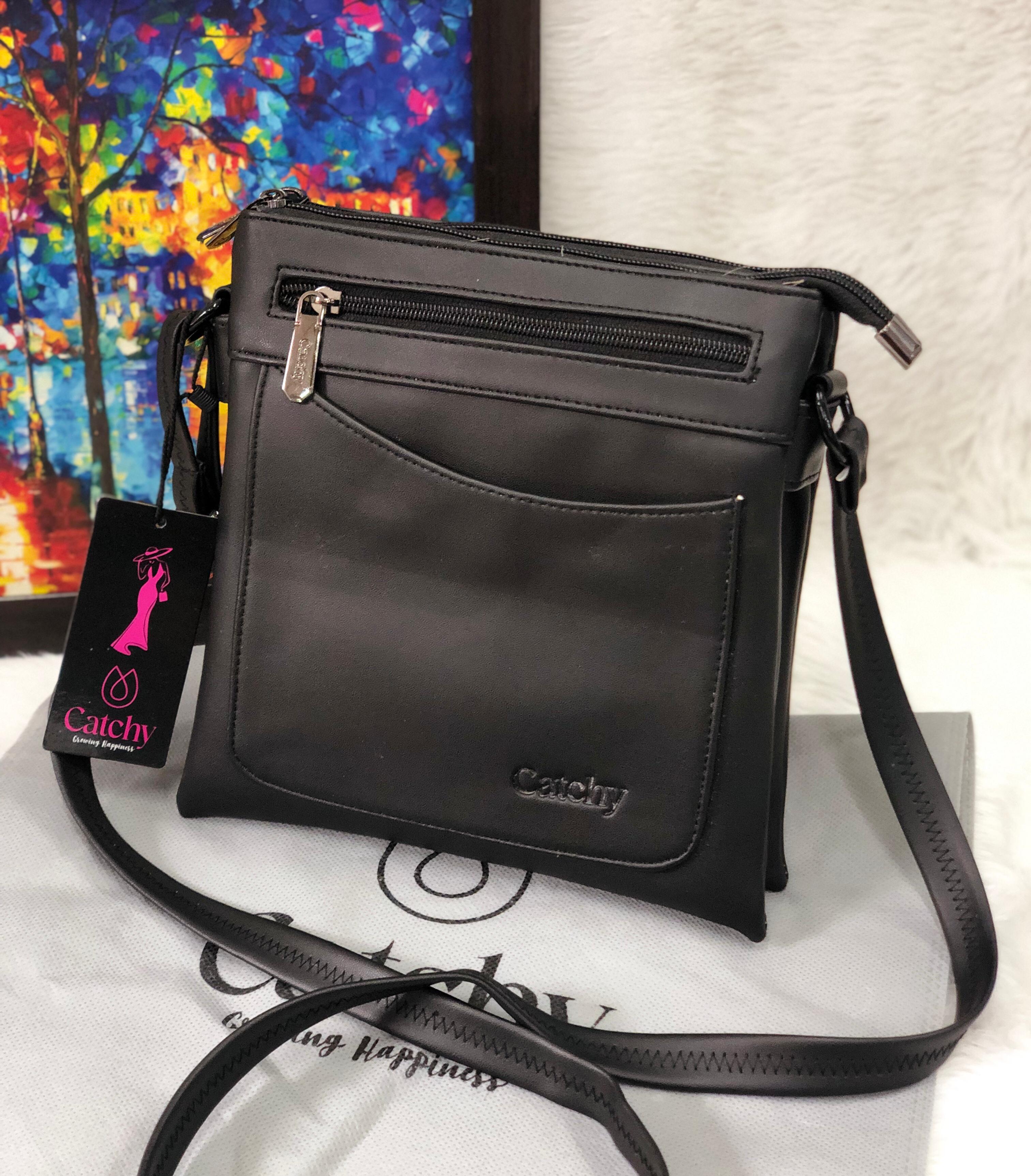 Black Catchy multi-compartment crossbody sling bag on a white fuzzy surface, with a colorful abstract painting in the background.