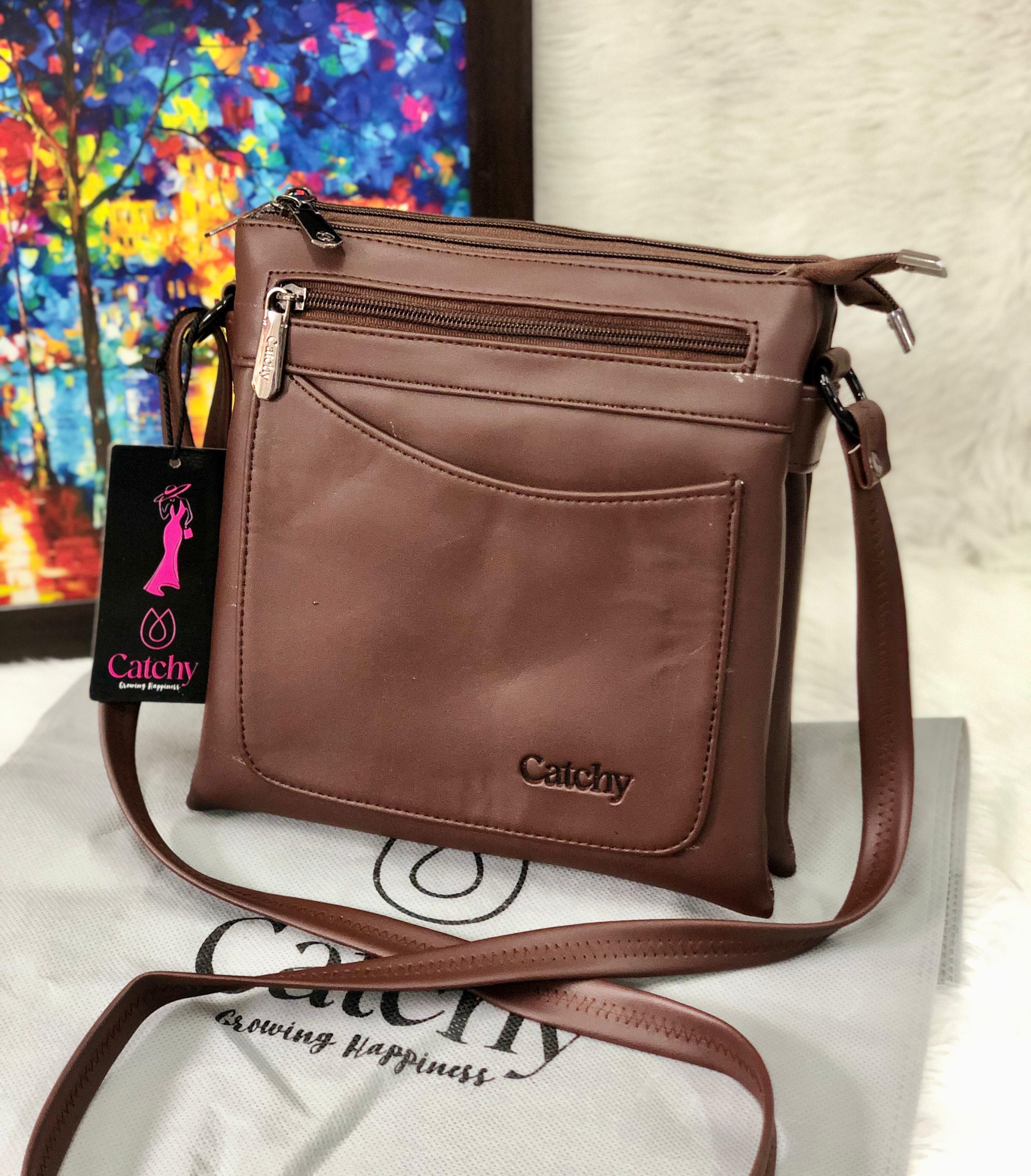 Brown Catchy multi-compartment crossbody sling bag on a white fuzzy surface, with a colorful abstract painting in the background.