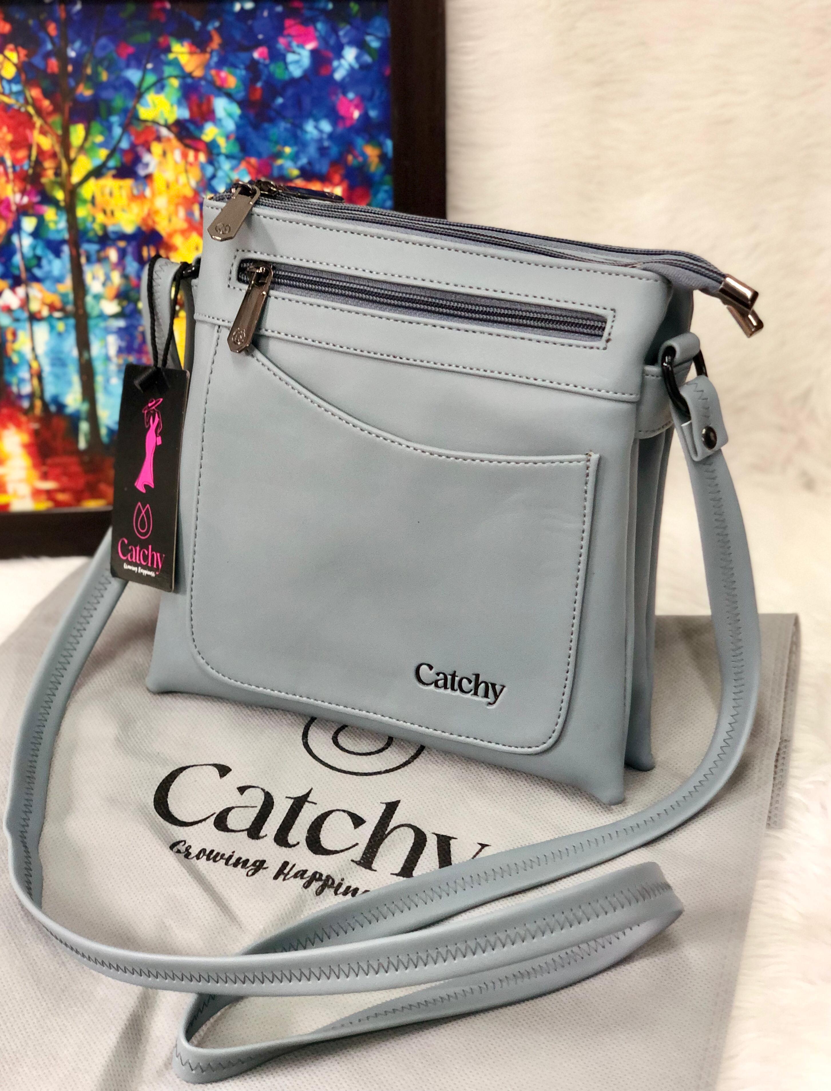 Light Blue Catchy multi-compartment crossbody sling bag on a white fuzzy surface, with a colorful abstract painting in the background.