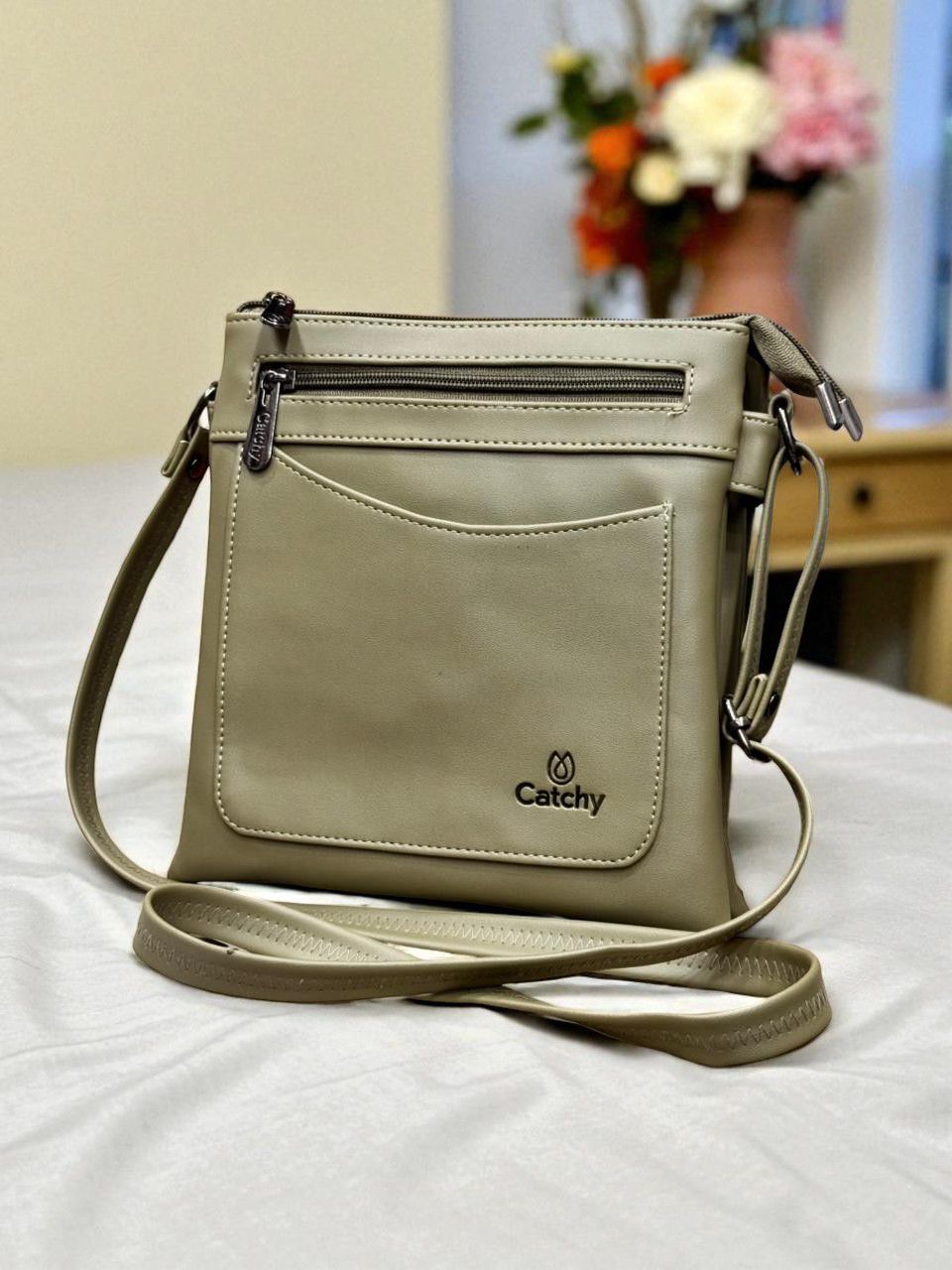 Olive Green Catchy multi-compartment crossbody bag in a home setting with floral decoration.