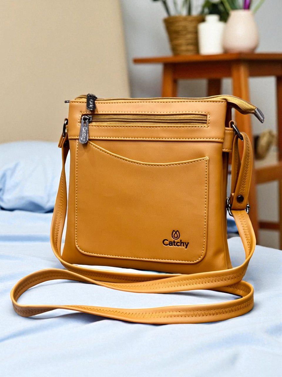Mustard Yellow Catchy multi-compartment crossbody bag on a blue bedsheet, in a bright room.