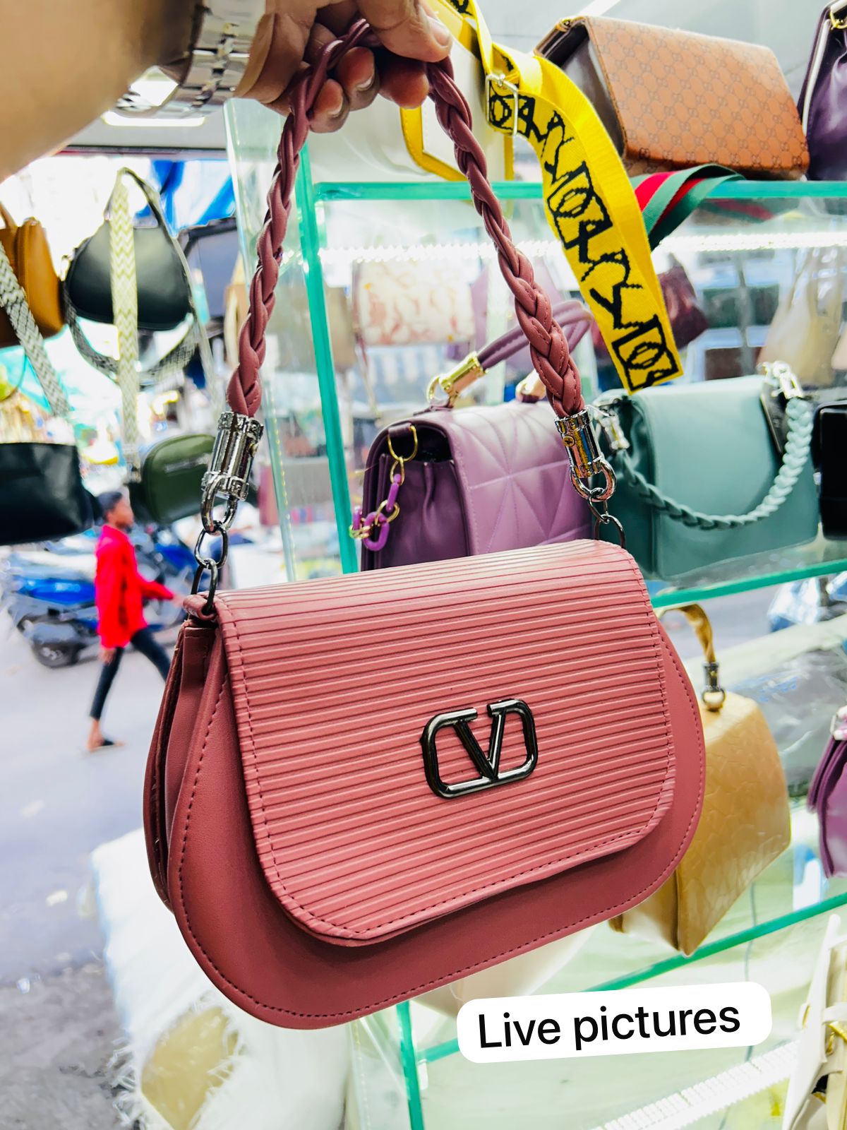 Live pic of TRENDBUY Vivid Pink crossbody bag held by hand, showcasing braided handle and V logo in a store setting.