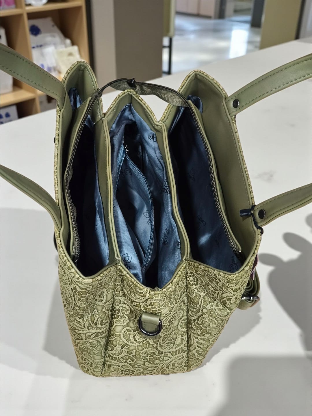 Close-up interior view of TRENDBUY floral embossed handbag showing three blue zippered compartments and ample storage.