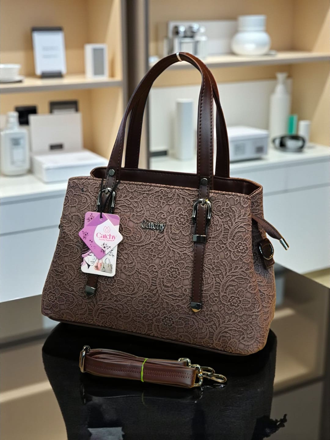 Rich dark brown floral embossed TRENDBUY handbag with its adjustable shoulder strap, elegantly placed on a reflective surface.