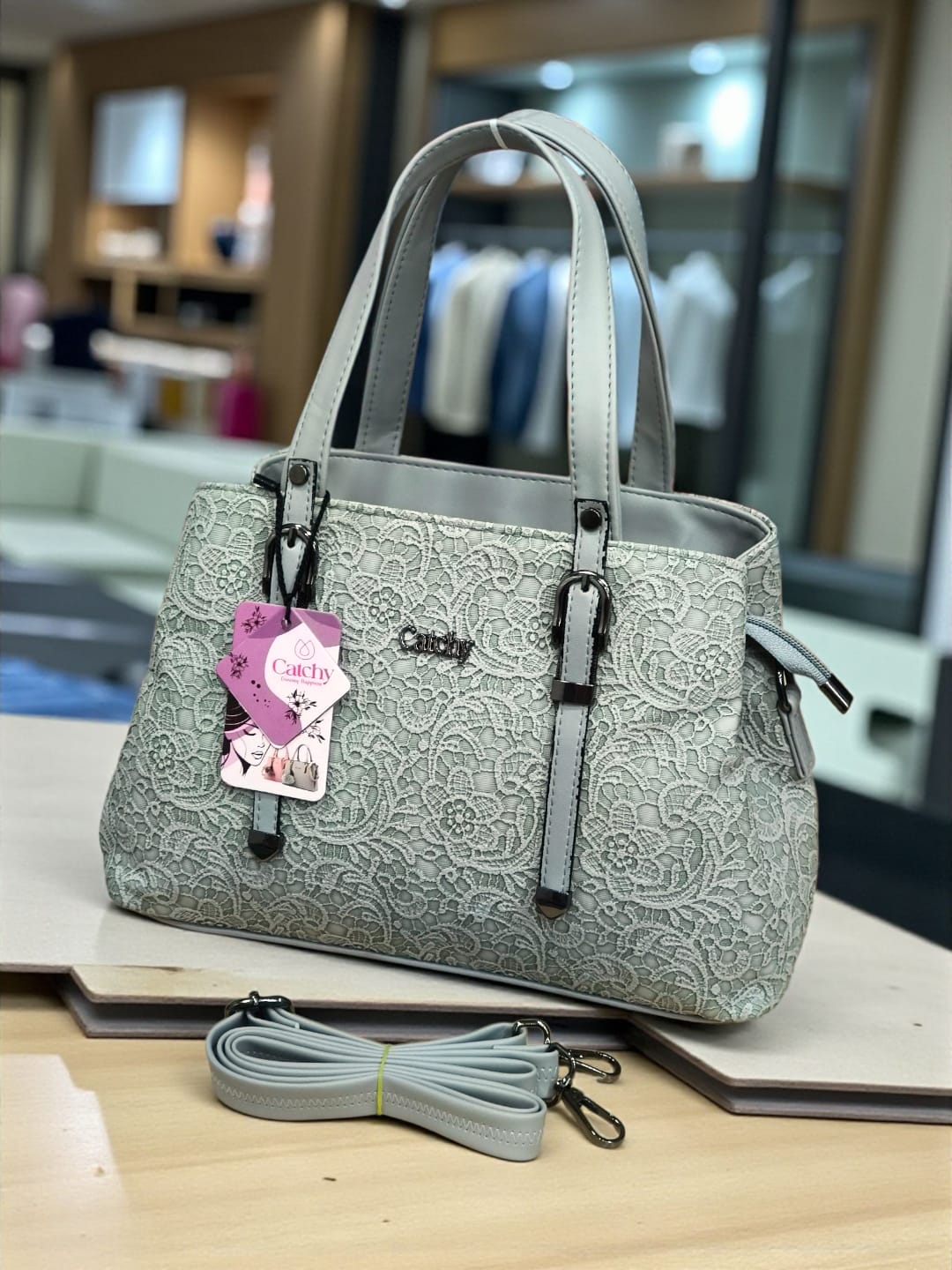 Sophisticated light blue-grey floral embossed TRENDBUY handbag with included sling strap, displayed in a modern retail setting.