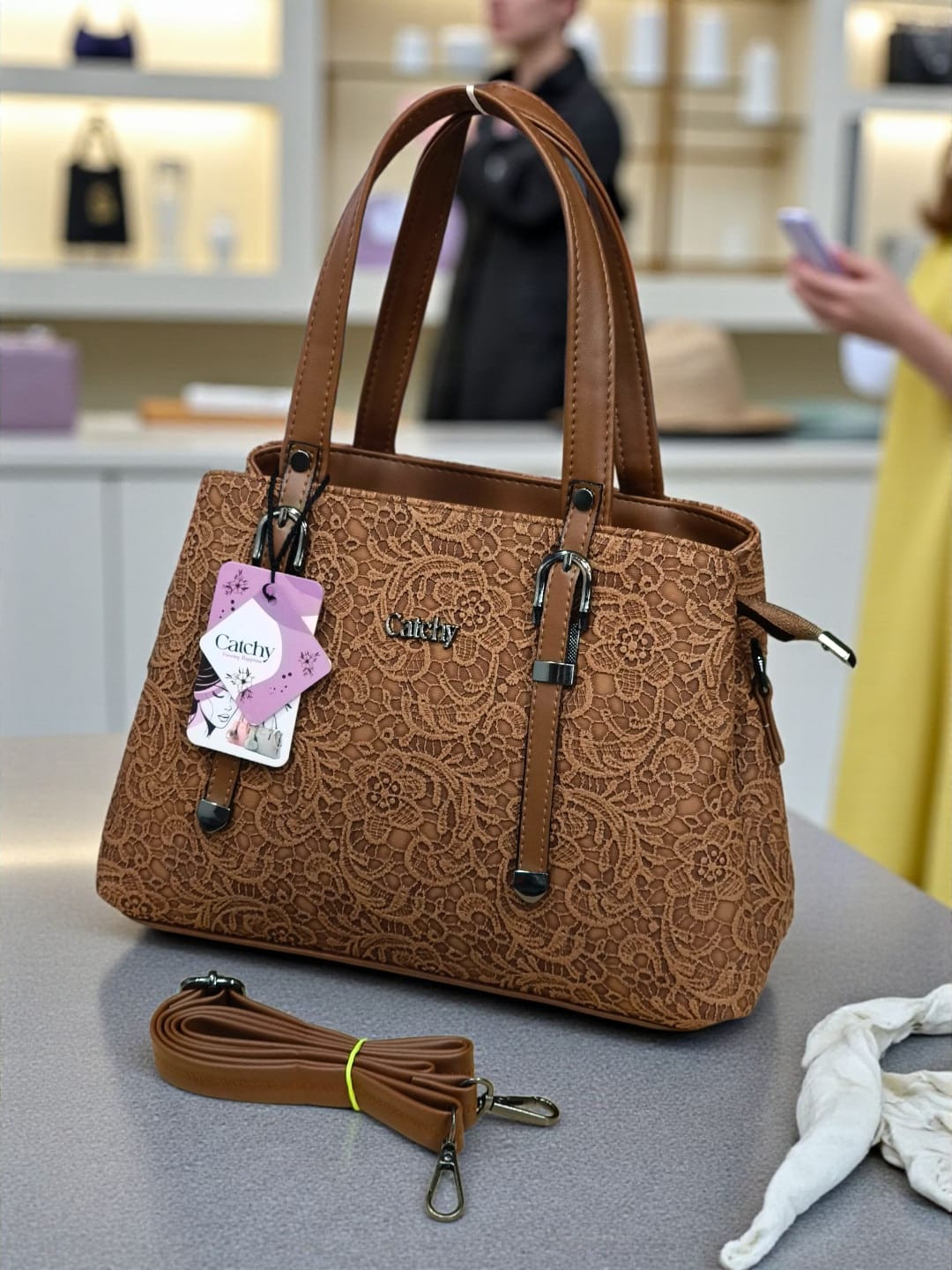 Warm tan floral embossed TRENDBUY handbag, featuring its matching adjustable strap, displayed in a bright retail environment.
