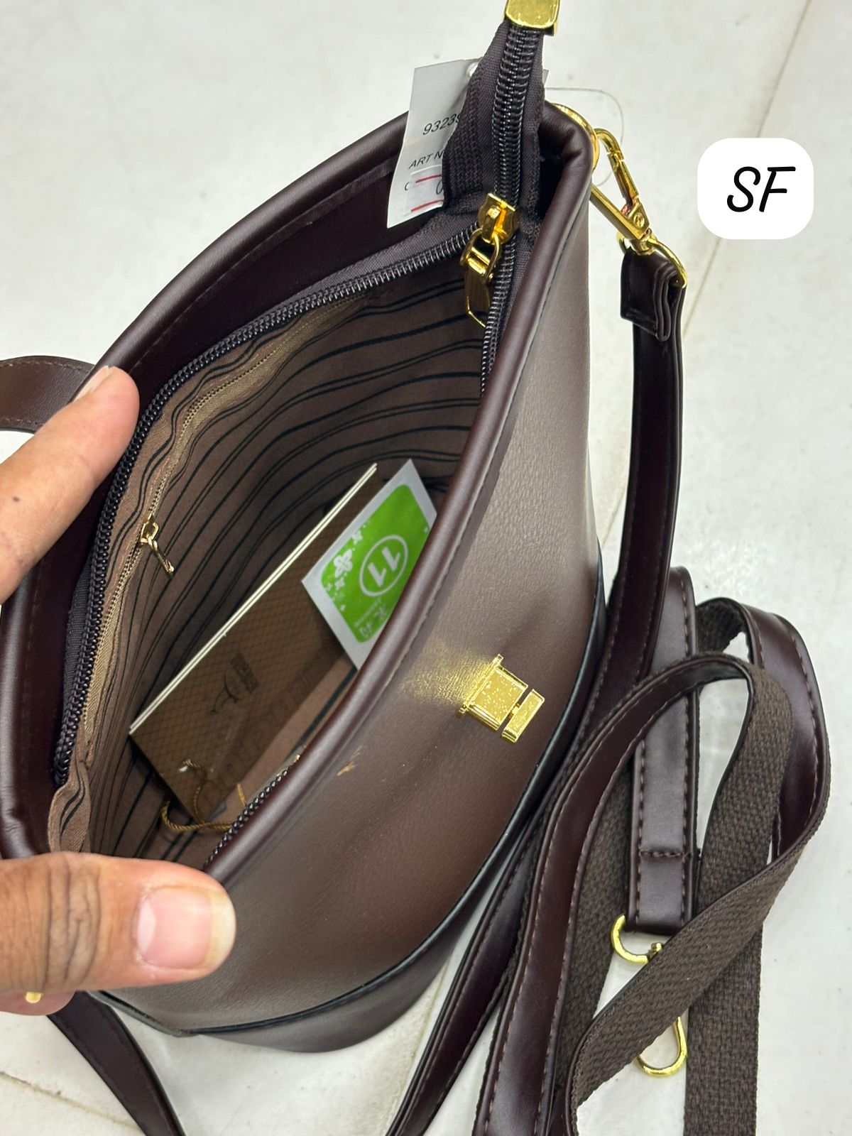 Interior view of the dark brown sling bag, revealing striped lining and zippered pocket.