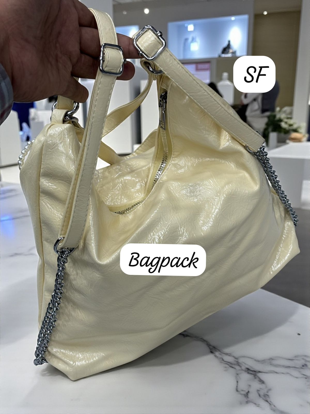 Close-up of the TRENDBUY cream convertible bag demonstrating its backpack configuration with silver chain detailing.
