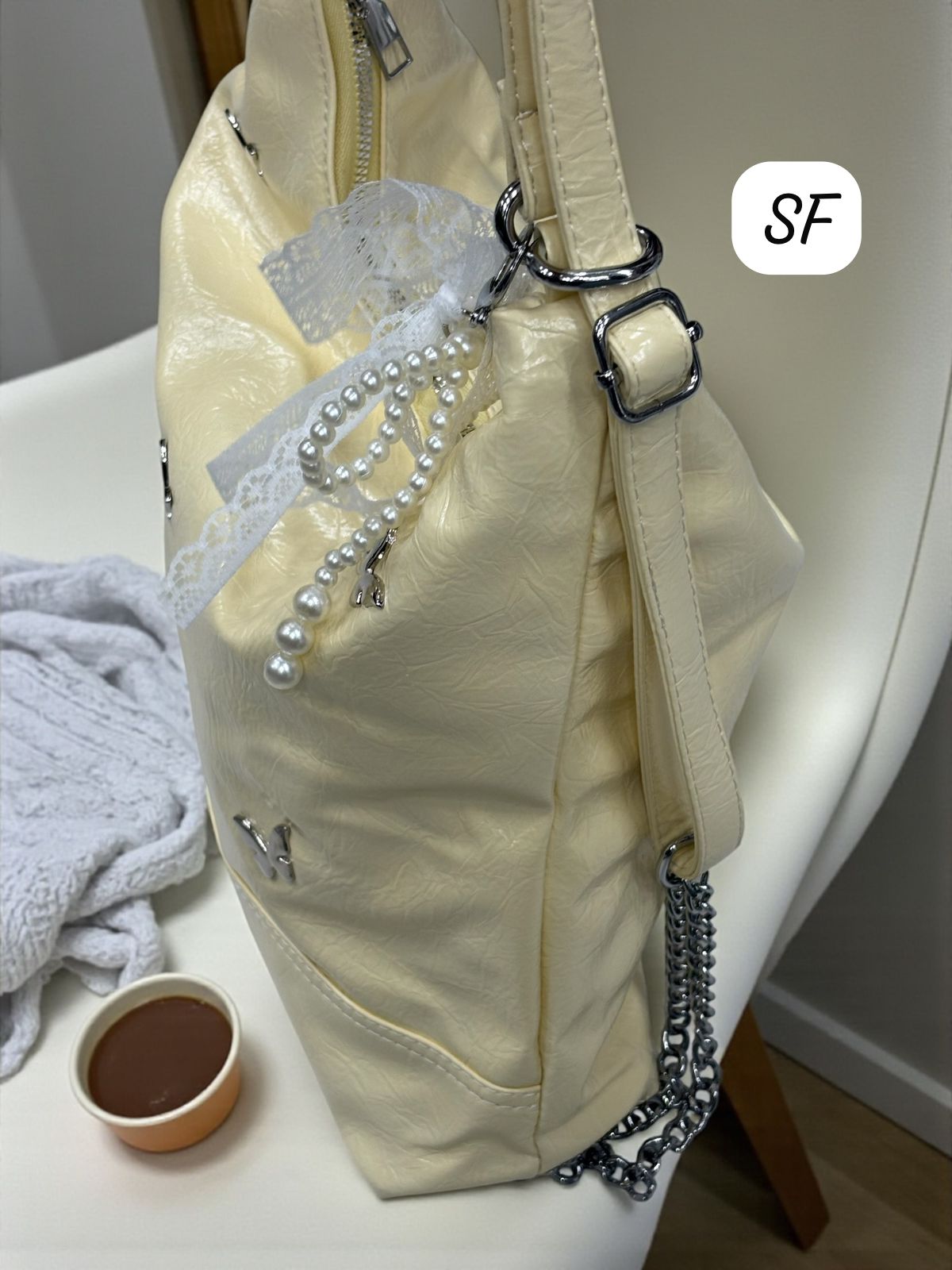 Side profile of the TRENDBUY cream convertible bag, highlighting the shoulder strap, chain detail, and lace-pearl charm.