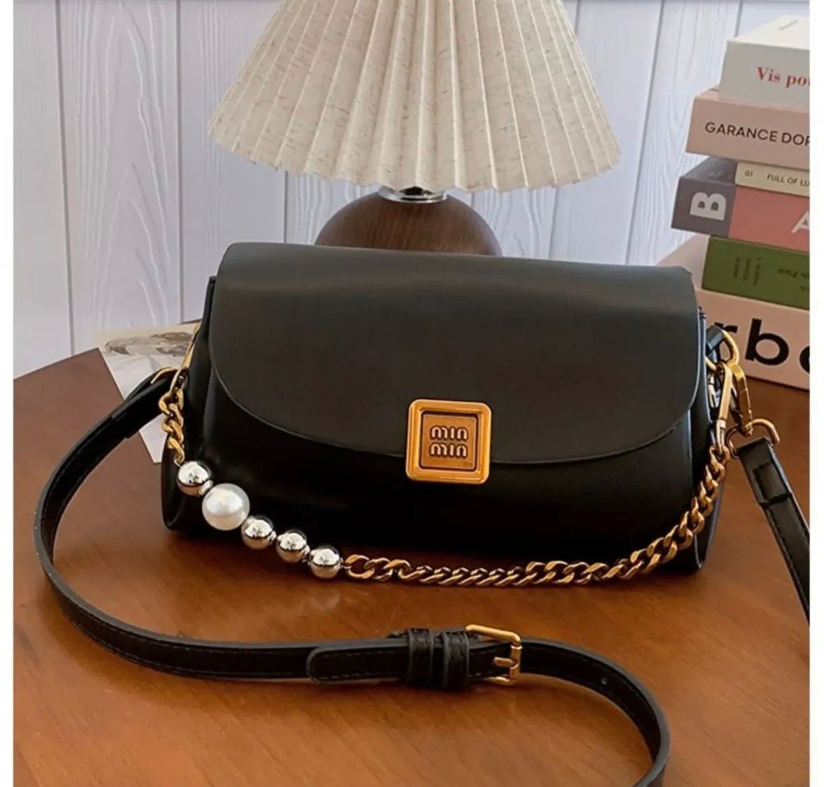 TRENDBUY Premium Broad Belt PU Slingbag in sleek Black, showcasing a gold metallic logo, elegant gold chain, and pearl embellishments, with an adjustable black strap on a wooden surface.