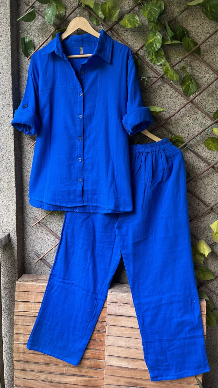 Vibrant Royal Blue Updown Mul Mul Cotton Cord Set, draped on a hanger with green foliage backdrop.