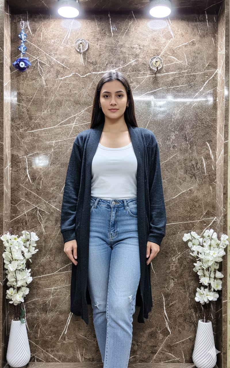 TRENDBUY model wearing a black knitted open-front shrug, white top, and blue jeans, standing in front of a marble wall.