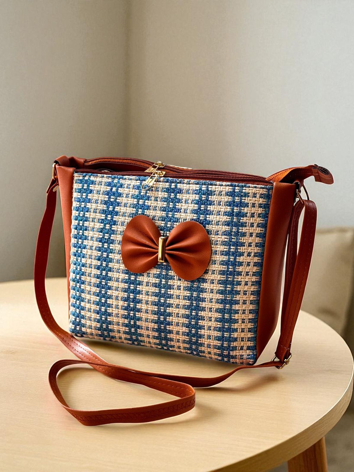 TRENDBUY blue and beige checkered bucket sling bag with a brown bow detail, on a wooden table.