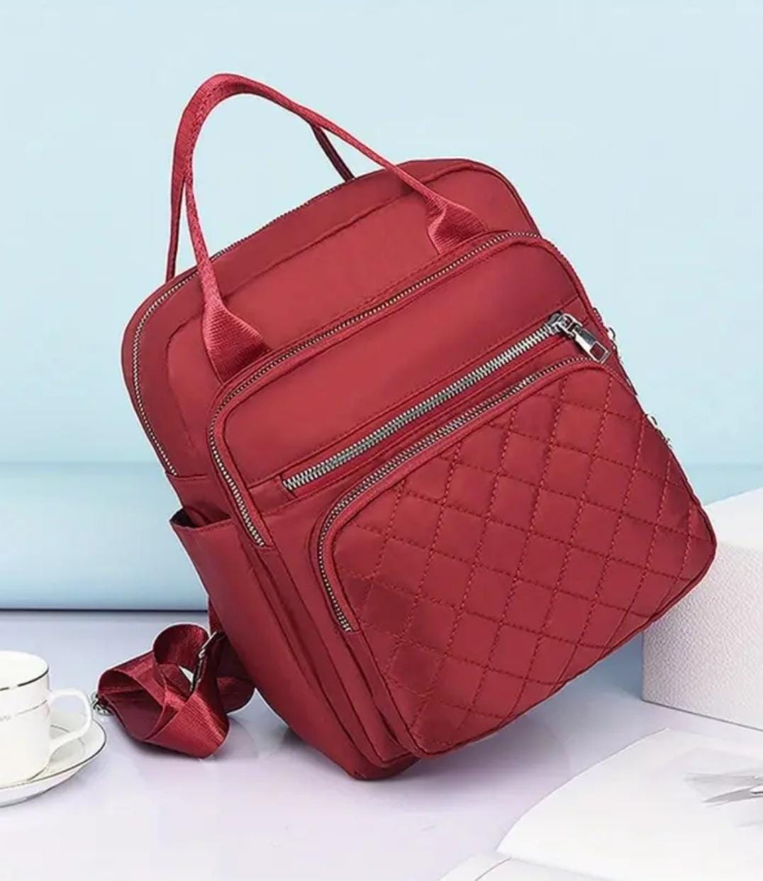 Angled view of a vibrant red quilted nylon convertible bag, styled on a clean surface.