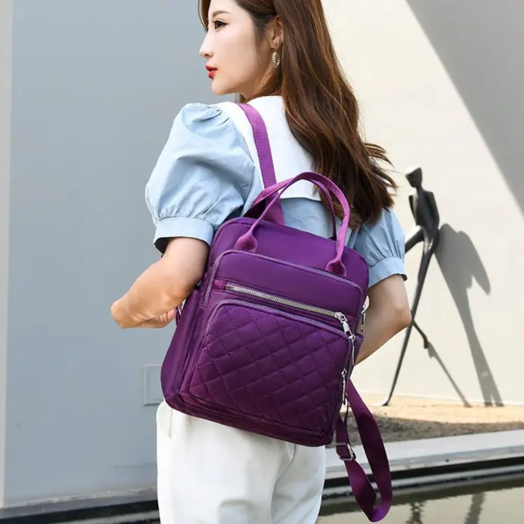 Woman stylishly carrying a purple quilted nylon backpack on her back outdoors.