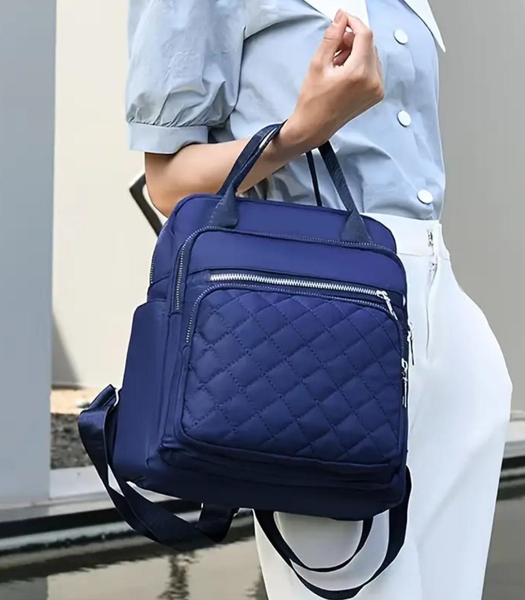 Woman demonstrating how to carry the navy blue quilted nylon backpack by its top handle, acting as a tote bag.