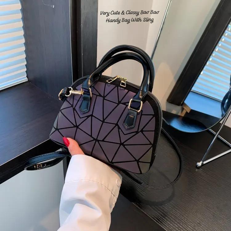 Hand holding an iridescent geometric Bao Bao dome handbag with a detachable sling, close-up on the quality material and finish