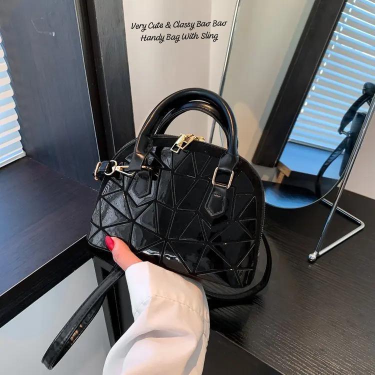 Close-up of a glossy black geometric Bao Bao mini handbag with black trim and sling, held by hand, showcasing its quality and design details