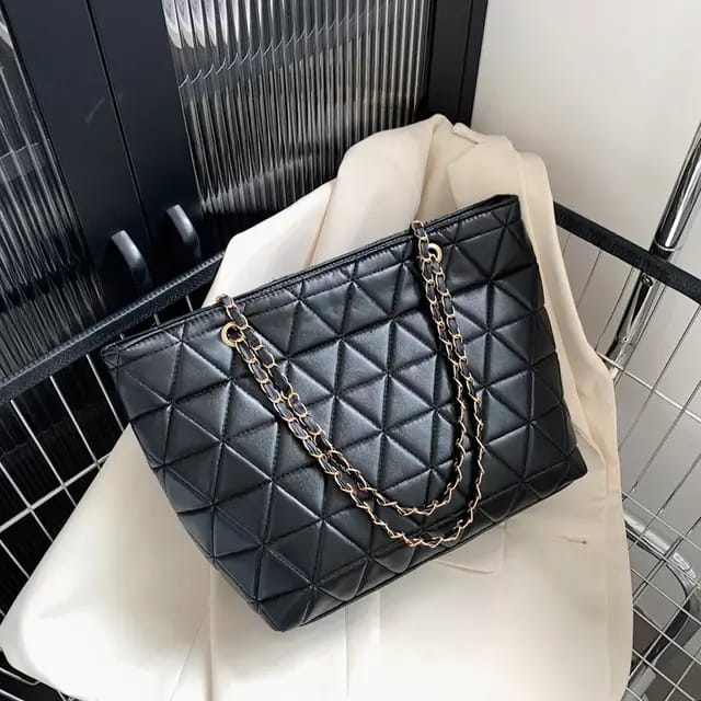 Close-up view of the TRENDBUY black rhombus quilted tote bag with double golden chain straps on a white blazer