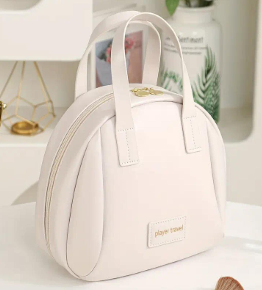 Elegant white 'player travel' cosmetic bag with a golden zipper and top handles on a modern white background.