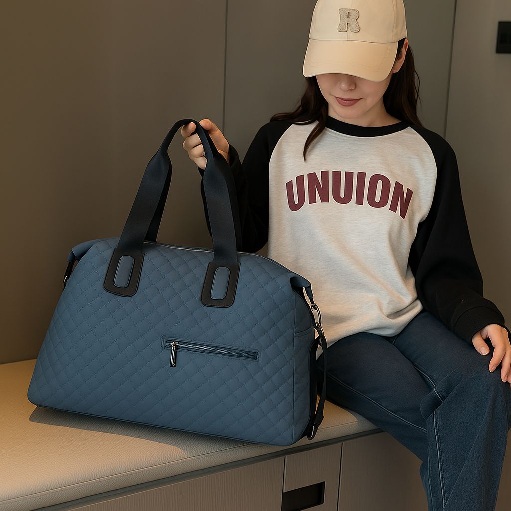 A person sitting on a bench, holding a large ocean blue quilted duffle bag, demonstrating its comfortable size and usability as a carry-on or personal item.