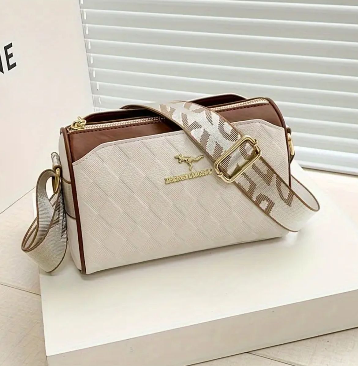 Angled view of TRENDBUY cream sling bag showing adjustable patterned strap and gold hardware accents.