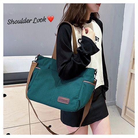 Woman modeling a teal (green) corduroy tote bag over her shoulder with a heart emoji indicating 'Shoulder Look'.