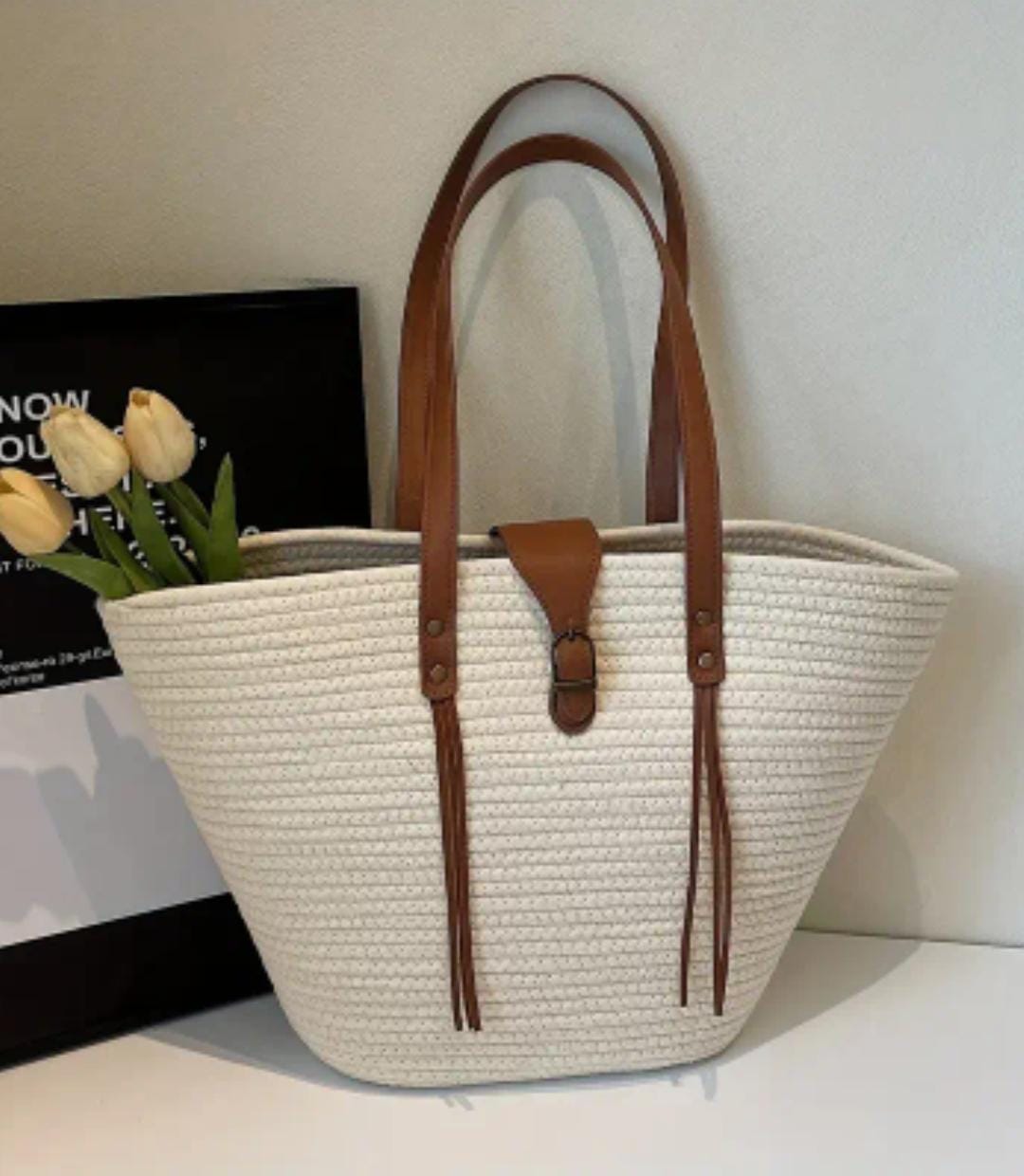 TRENDBUY white straw weave tote bag with brown faux leather handles and buckle, front view with yellow tulips.