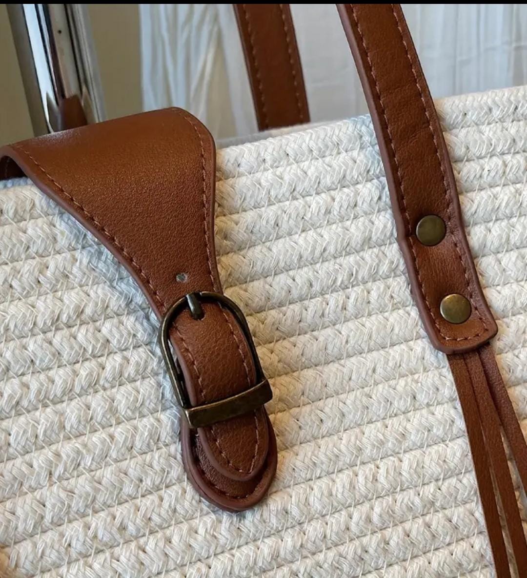 Close-up detail of the white straw weave tote bag's brown faux leather buckle closure and sturdy handle rivet.