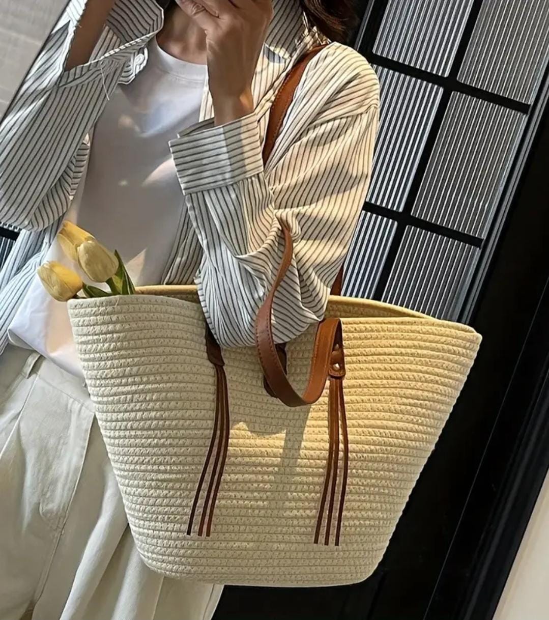 Lifestyle shot of a woman carrying the TRENDBUY beige straw tote bag over her shoulder, styled with a striped shirt.