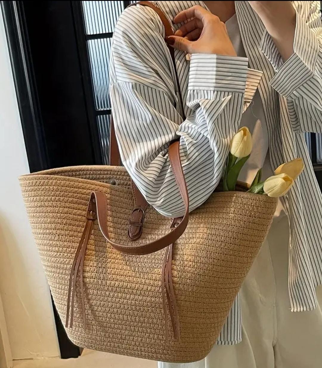 Woman's hand holding the TRENDBUY beige straw tote, revealing its spacious opening with yellow tulips peeking out.