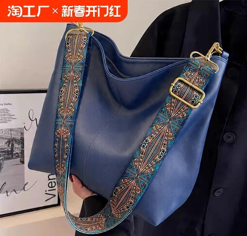 Model wearing a navy blue outfit holding a blue TRENDBUY PU leather tote bag with an intricate decorative shoulder strap, indoors.