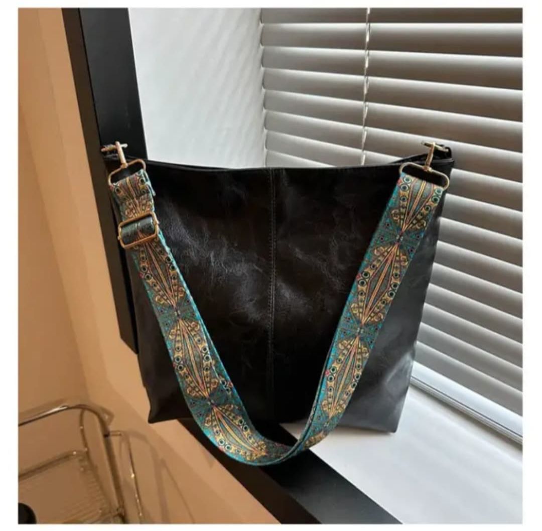 Close-up of a black TRENDBUY PU leather tote bag showcasing its decorative teal and gold patterned shoulder strap by a window.