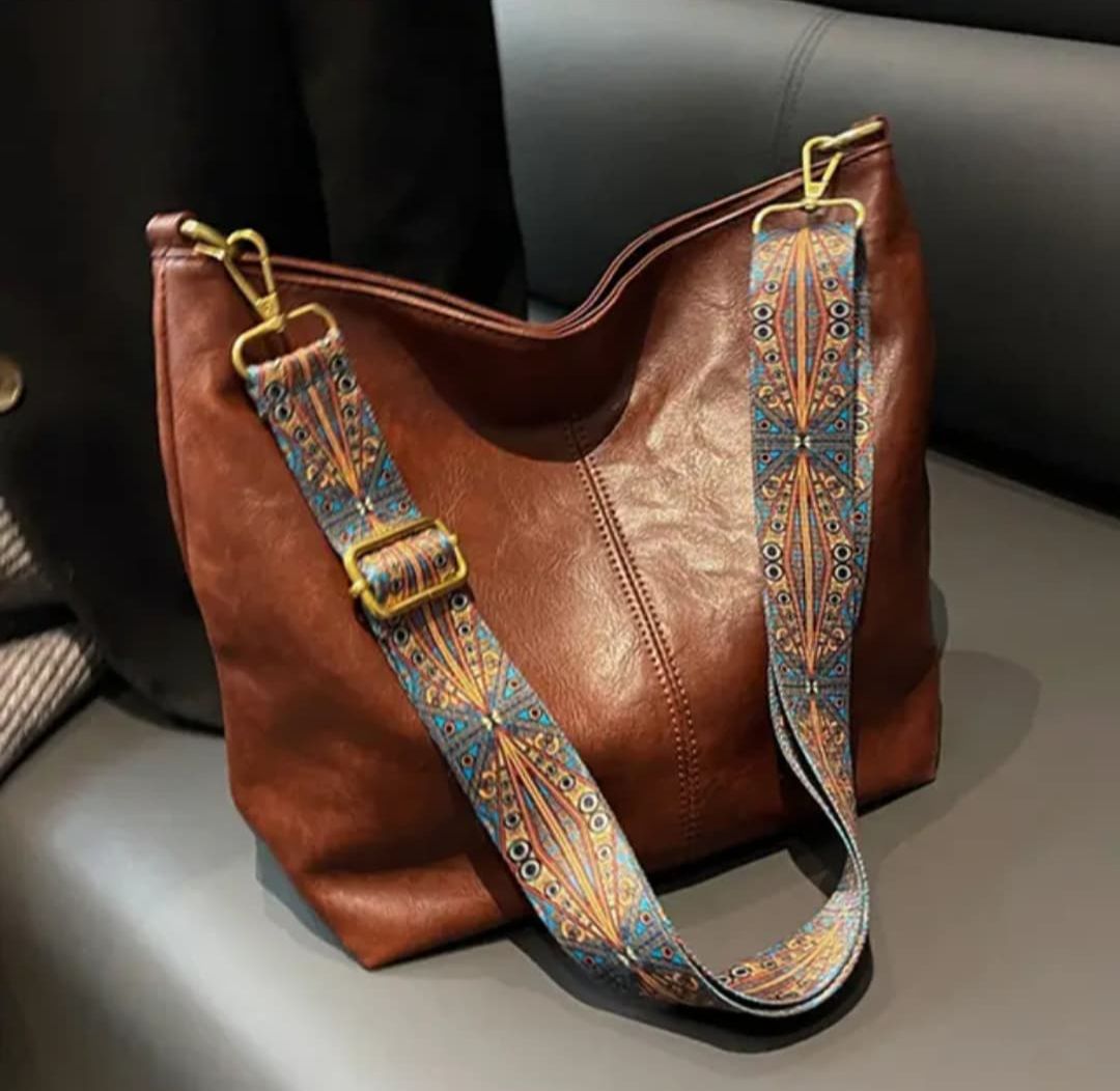 Rich brown TRENDBUY PU leather tote bag with a strikingly colorful, patterned shoulder strap, resting on a sofa.