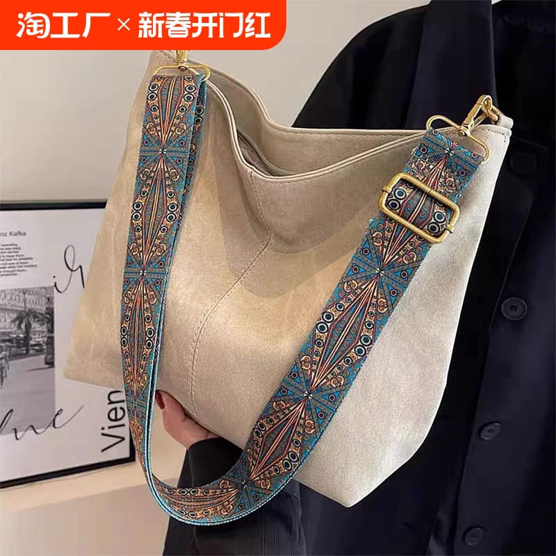 Model wearing a navy blue top, holding a beige TRENDBUY PU leather tote bag with a decorative blue and gold strap, indoors.