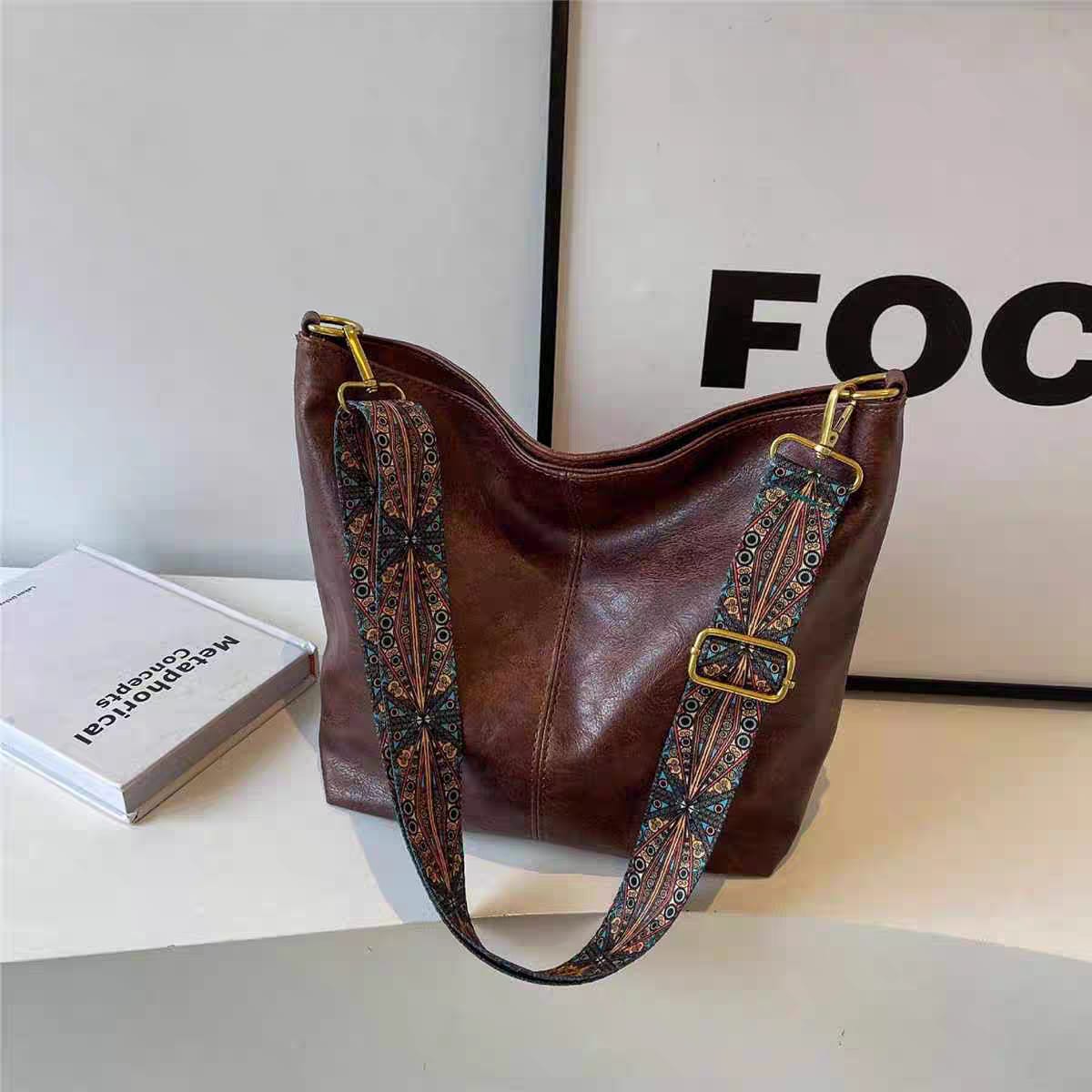 Elegant brown TRENDBUY PU leather tote bag with a decorative multi-color strap, sitting on a white desk with a framed art piece in the background.