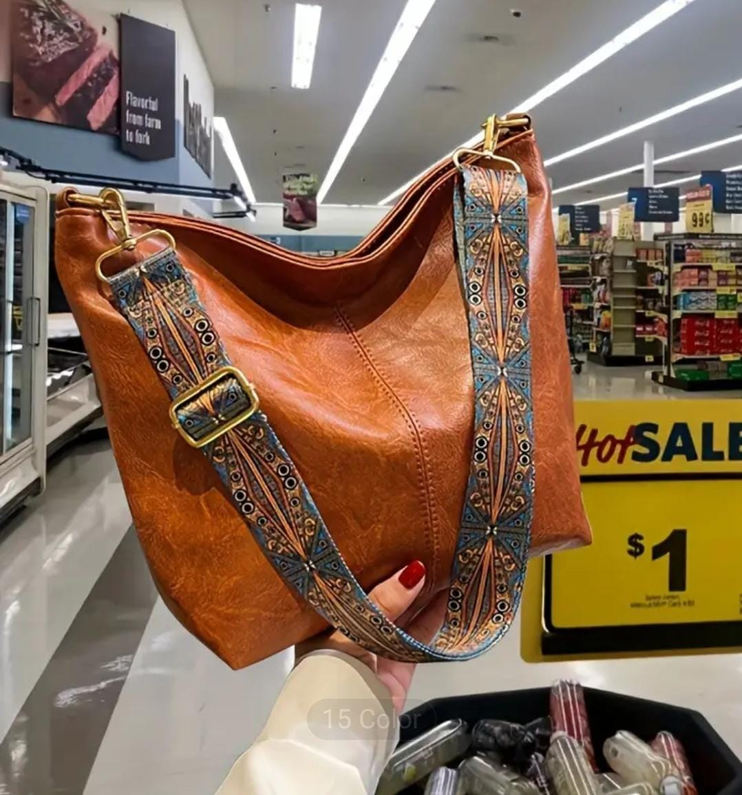 Person holding a brown TRENDBUY PU leather tote bag with a vibrant decorative strap, in a brightly lit grocery store aisle.