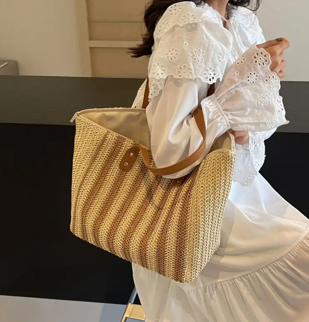 Woman wearing a white dress, elegantly carrying a khaki striped jute tote bag on her shoulder.