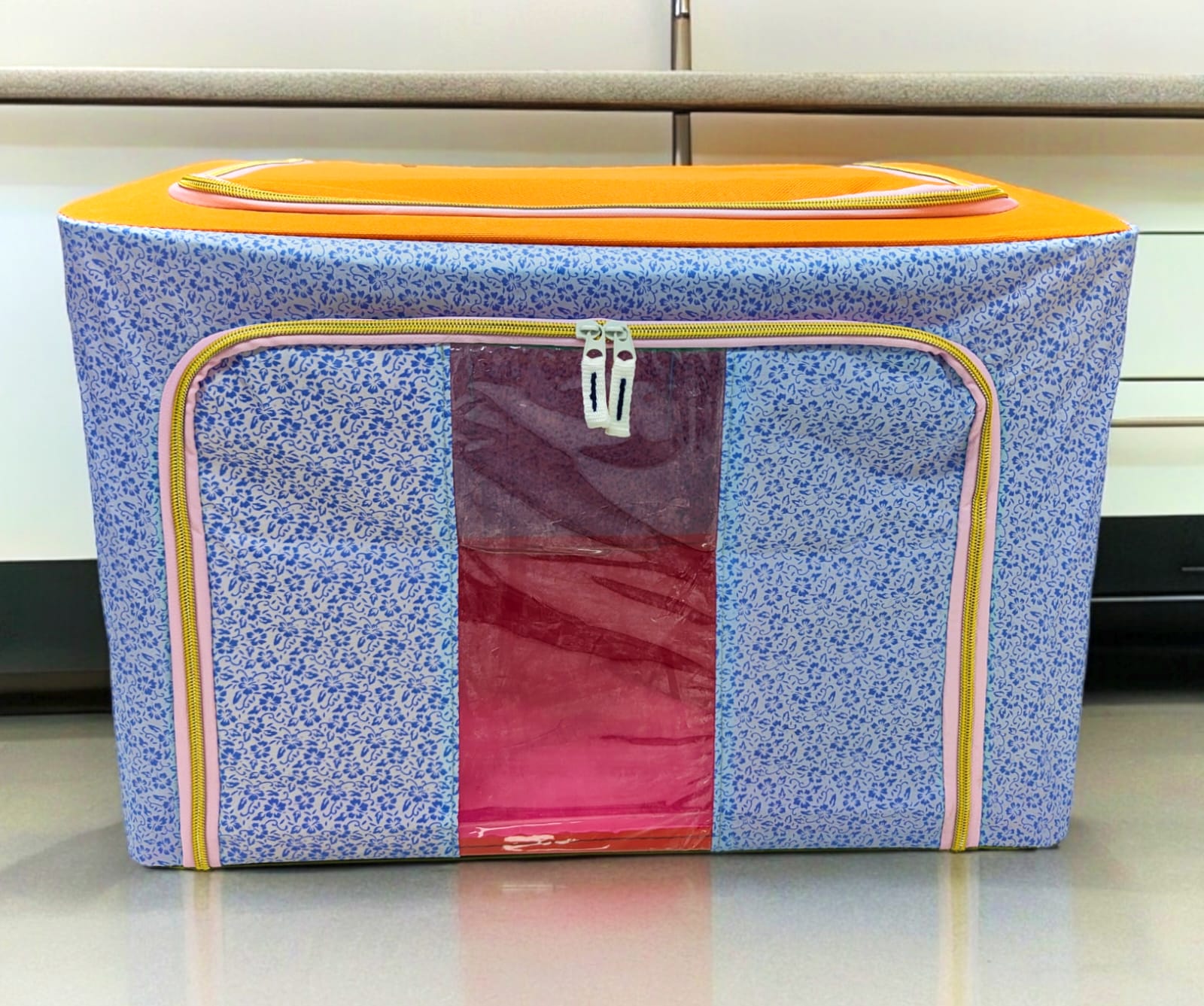 Blue floral patterned fabric storage box with orange top and yellow zippers, front view.