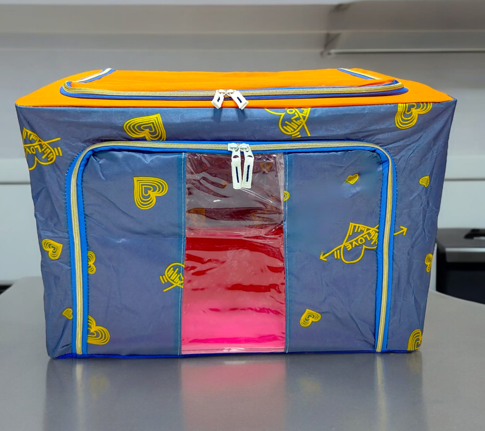 Grey storage box with yellow heart and 'LOVE' patterns, orange top, blue zippers, showing front access.