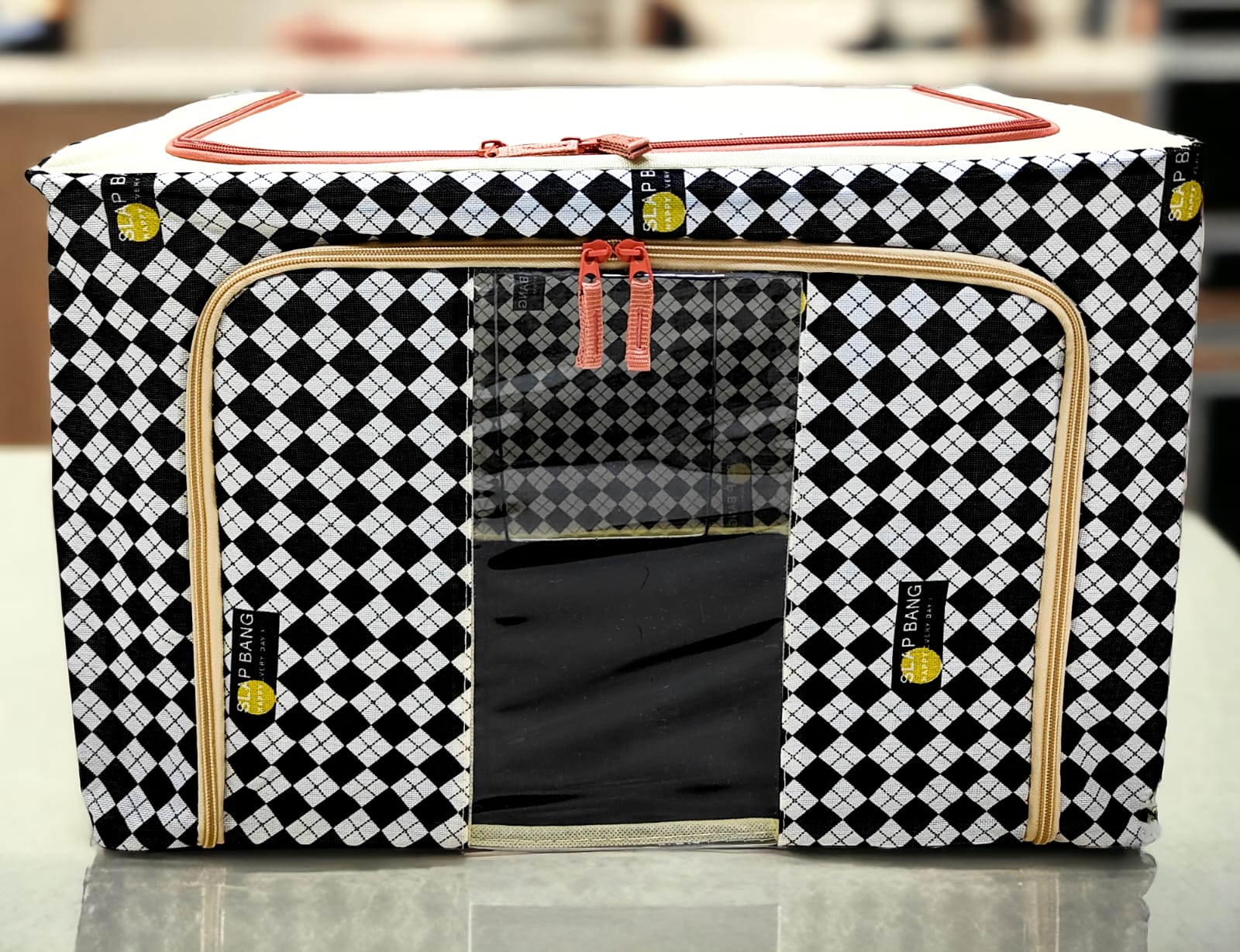 Black and white argyle patterned storage box with tan zippers and red pulls, close up on front panel.