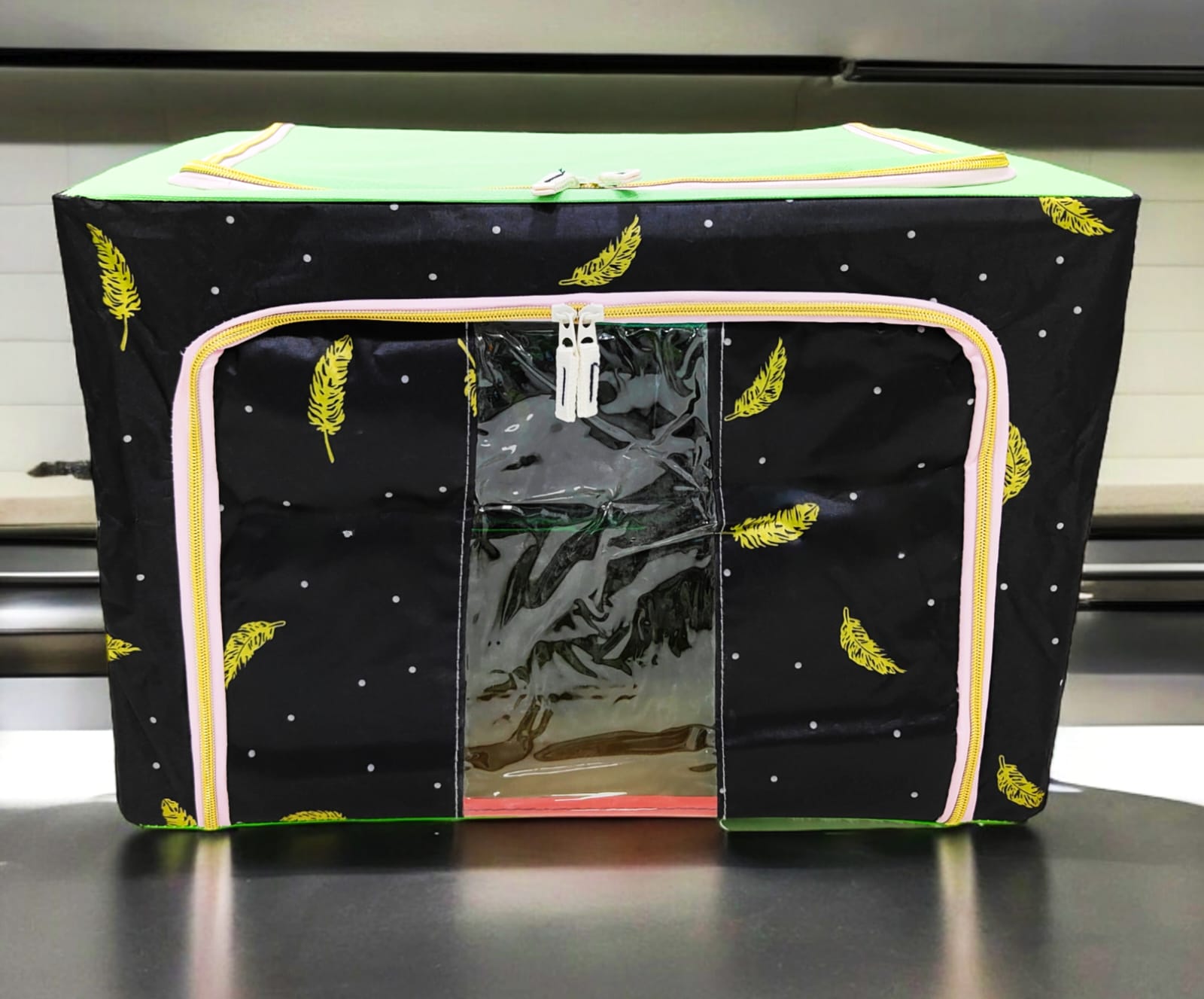 Black storage box with yellow feather patterns, light green top, pink zippers, displaying clear window.