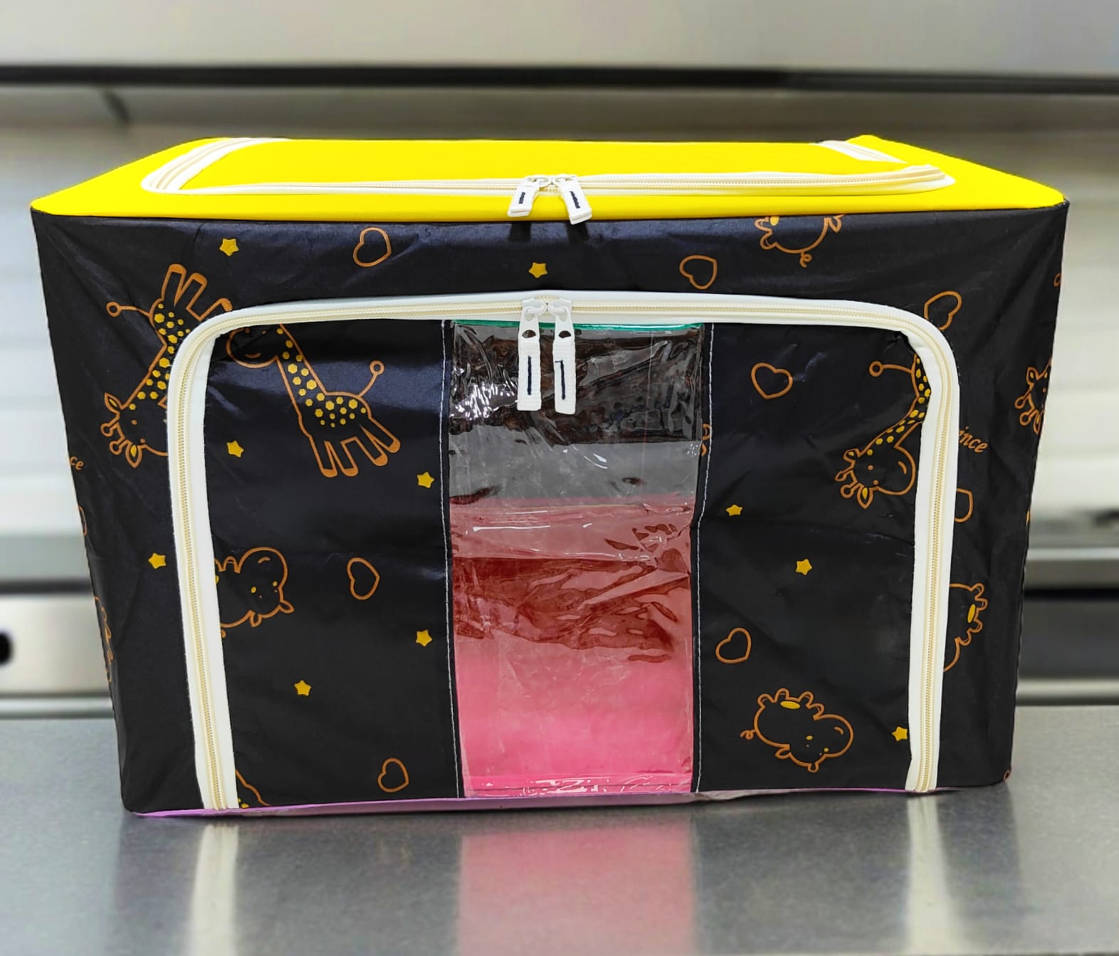 Black storage box with orange giraffe and star patterns, yellow top, white zippers, detail on print.