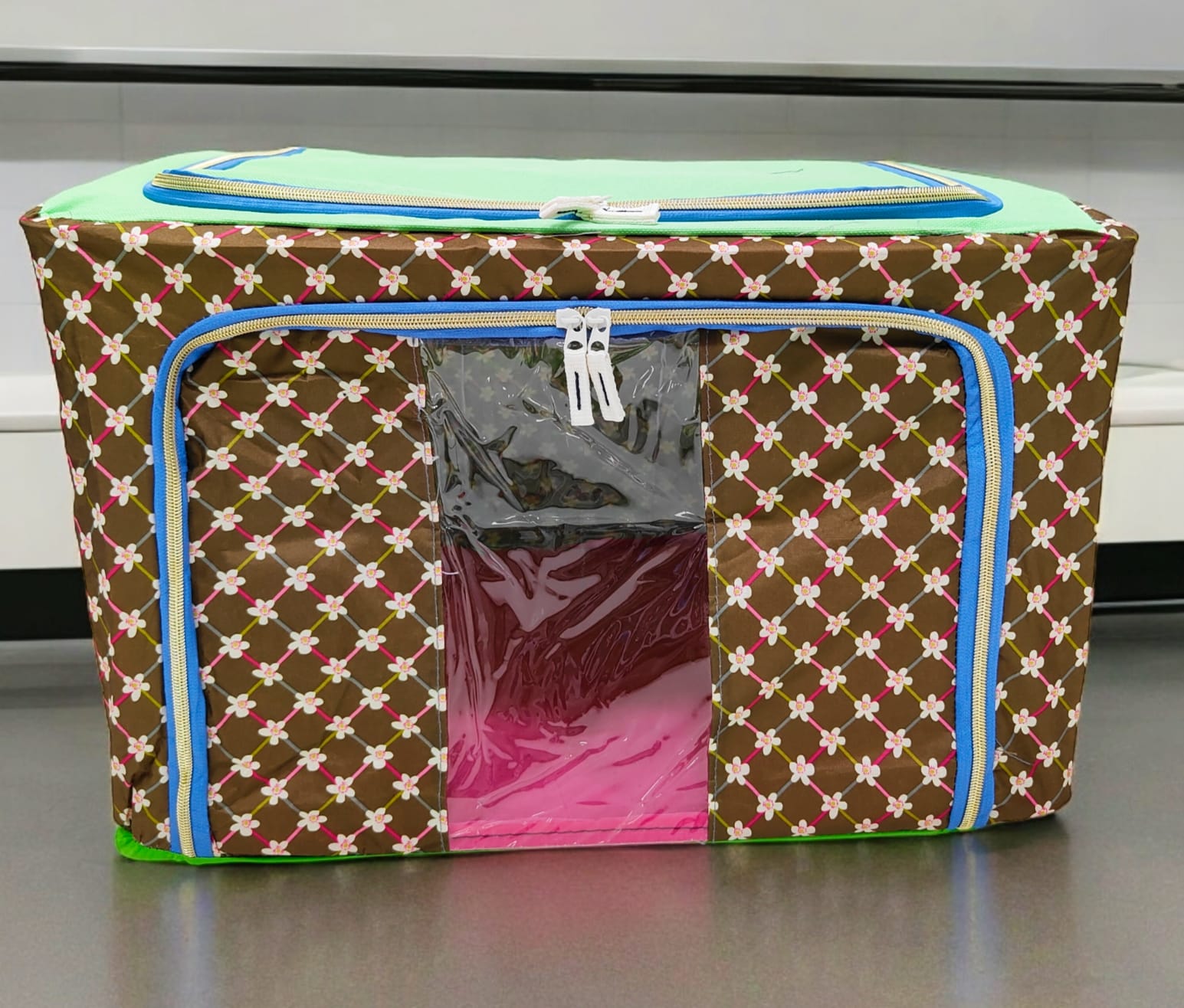 Brown storage box with small colorful flower patterns, light green top, blue zippers, from a slightly elevated view.