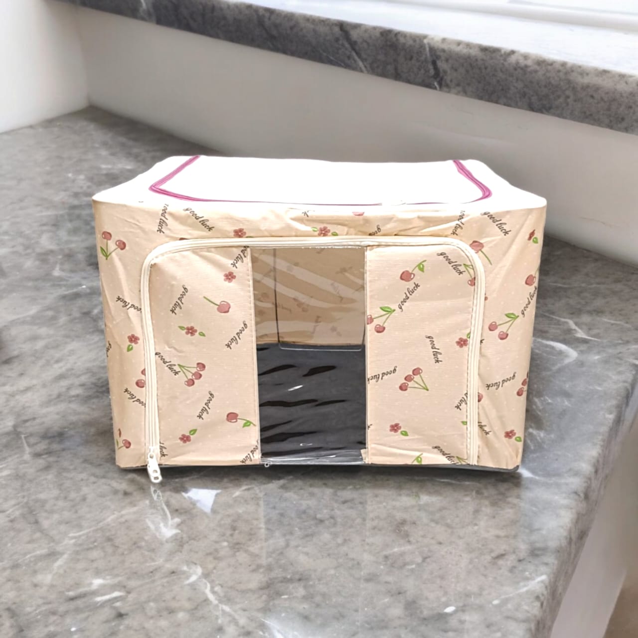 Beige storage box with cherry and 'good luck' text patterns, clear window, placed on a kitchen counter.