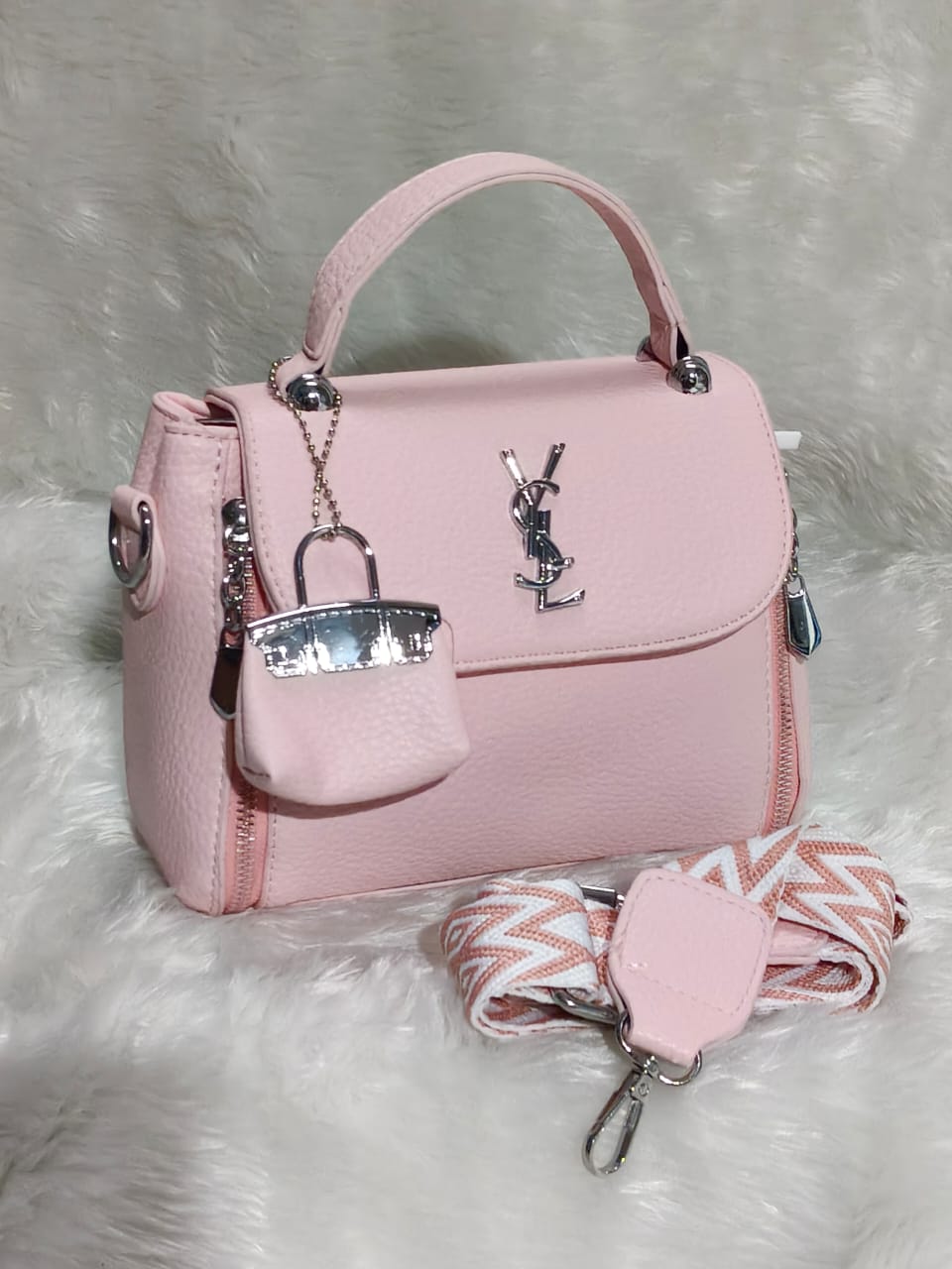 TRENDBUY premium YSL-style sling bag in soft pink, featuring silver hardware, a mini bag charm, and a patterned strap on a white furry background.