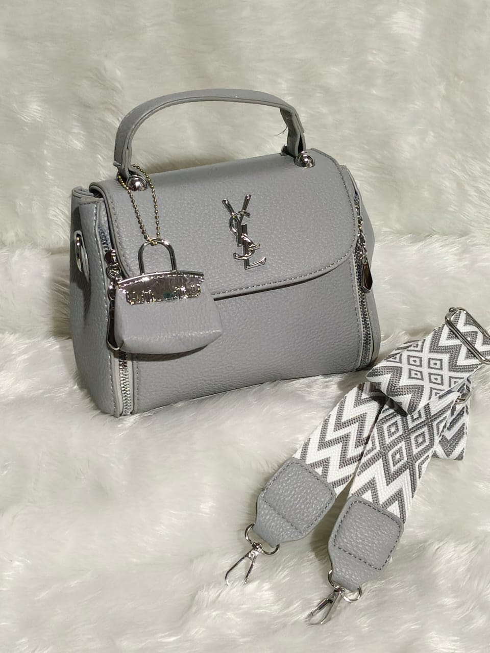 Chic grey TRENDBUY premium quality sling bag with silver logo, small charm, and a stylish grey and white chevron patterned shoulder strap.
