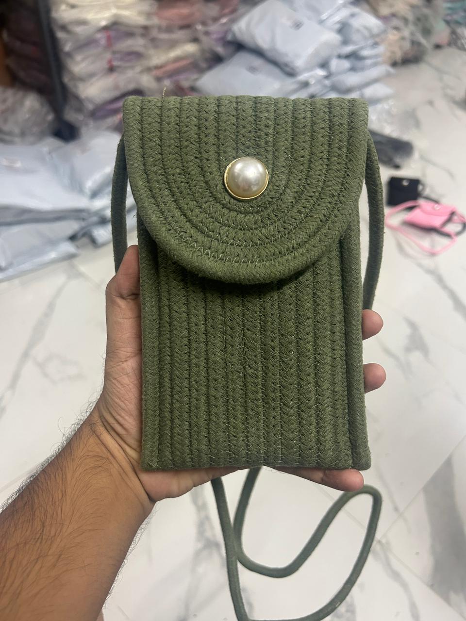 Green braided crossbody phone bag with pearl button flap closure, held in hand.