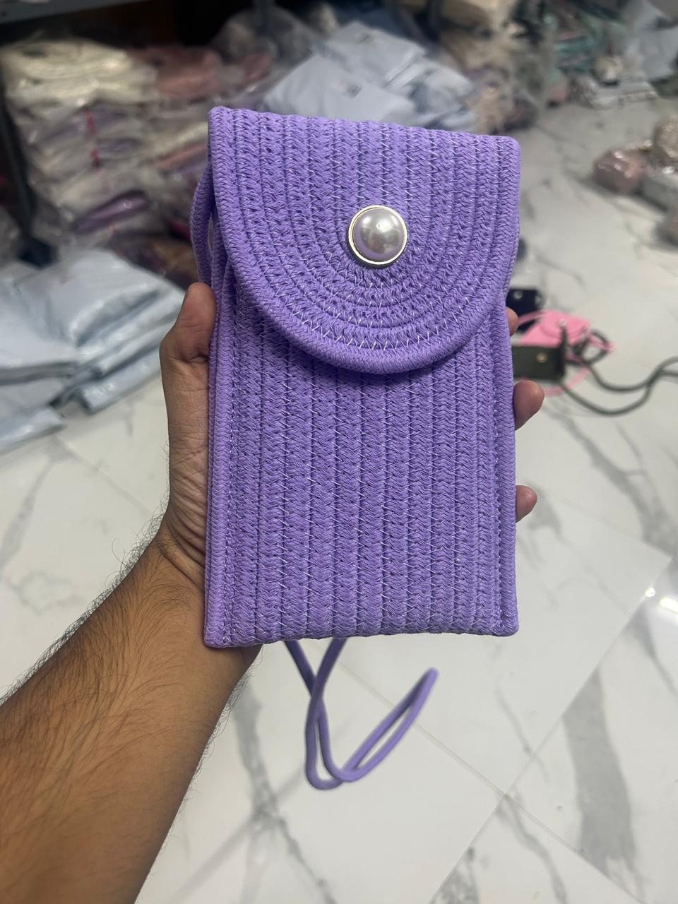 Purple braided crossbody phone bag with pearl button flap closure, held in hand.